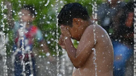 A boy cools off in the waters of a fountain during hot weather in San Salvador.