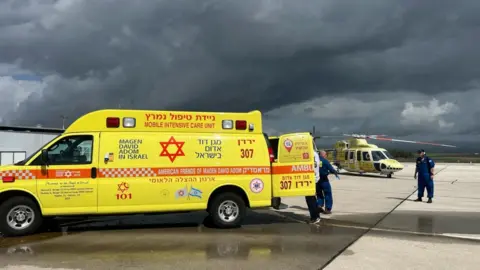 Yellow ambulance with helicopter in the background