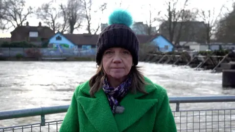 Liz Bentley standing next to the River Thames in a green coat