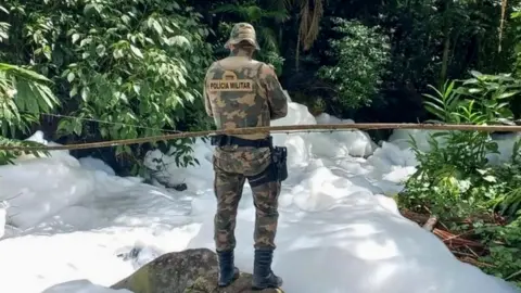 A military police officer stood in front of the contaminated river, surrounded by trees