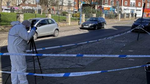 Police forensic teams photograph a street within a police tape cordon in Bristol