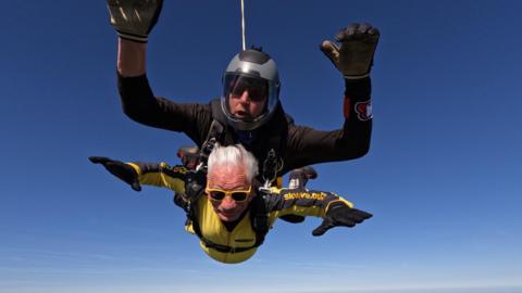 John Landau freefalling through the air, with a man strapped to his back