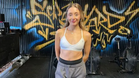 Mia Collins wearing a white sports bra and grey jogging bottoms