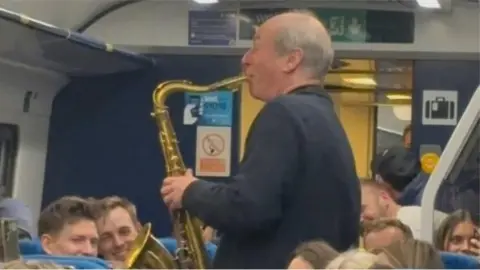 Man playing saxophone for train passengers