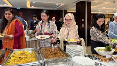 Members of Jersey's Muslim community serve themselves traditional foods from buffet trays to celebrate Eid