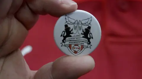Michael McWilliams holding up a badge, showing the crest of the Harvey McWilliams Foundation