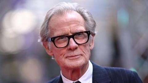 Actor Bill Nighy wears a smart navy pinstripe suit and bold black glasses on the red carpet at the London Film Festival