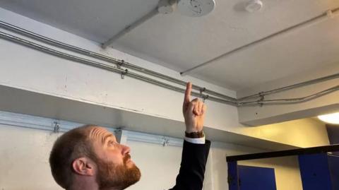 Head teacher Matt Carpenter points at a vaping sensor installed on the ceiling in the school toilets