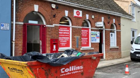 Facade of Framlingham post office with an industrial skip outside on the road