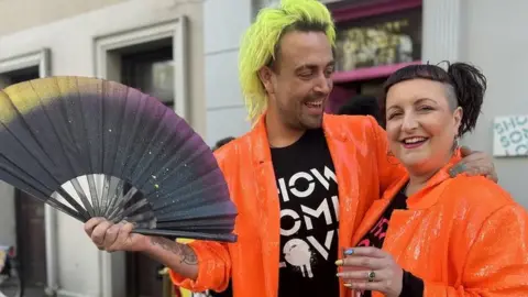 Connor Kerr holding a fan and Becky Bellamy - both wearing orange sequin jackets