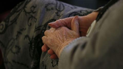 An elderly person's hand resting on their leg.