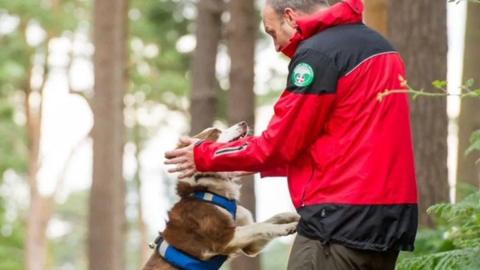 A man in a red jacket bending down and speaking to a dog