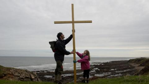 A photograph from the 1980s with Nadia and Pete Coppola erecting a wooden cross by the sea
