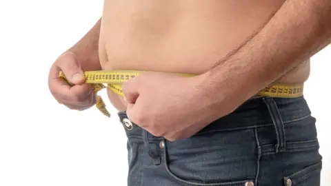 Barechested man measures waist with measuring tape