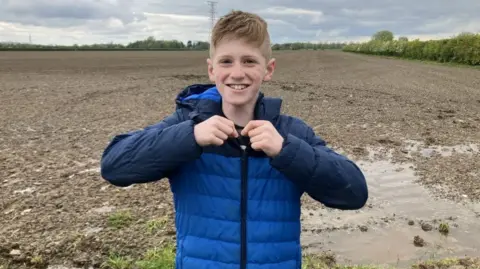 Boy in blue puffa jacket holds up tiny bit of metal with field in background