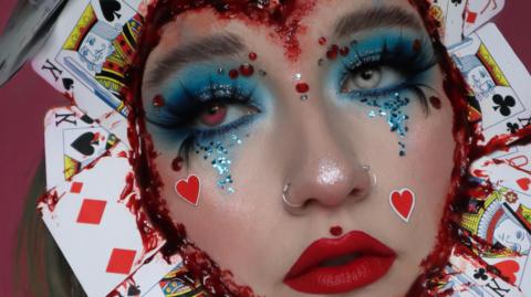 Close up shot of Beckii's face with glittery blue eyes, hearts on her cheeks and a ring of playing cards around her face