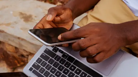 Stock photo of a student with laptop and phone in Tema, Ghana