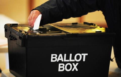 Picture of a ballot box with a hand holding a paper above
