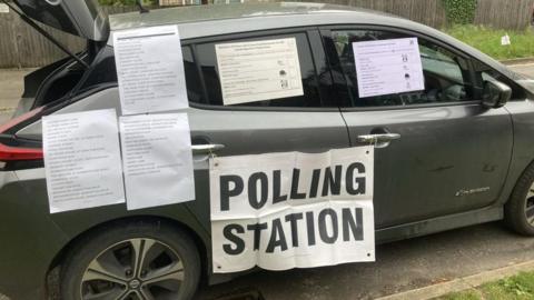 The car with a polling station sign stuck to it