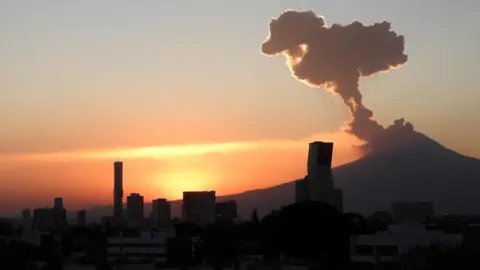 Volcano spewing ash and smoke over a city skyline at sunrise