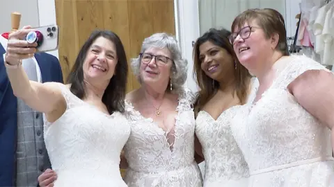 Four women in wedding dresses take selfie