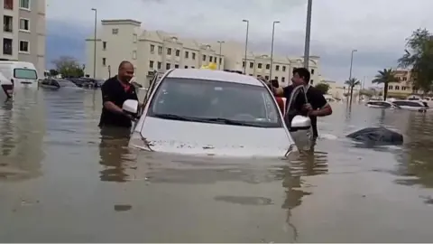 Men stand by a car that's submerged in water