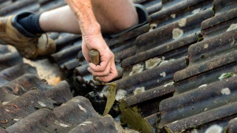 The hands and feet of a roofer seen as they work on a tiled roof