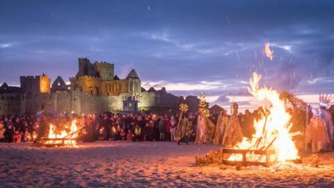 A crowd on Peel Beach as people perform by fire pits