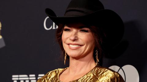 Shania Twain, wearing a black cowboy had and gold top