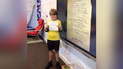 Cadell holding Sir David's letter and standing in front of the board in class