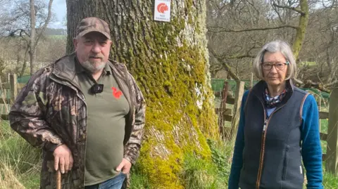 Ian Glendinning and another member of the Coquetdale Squirrel Group standing in front of a tree 
