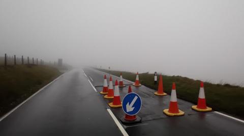 Traffic cones surrounding a section of the Mountain Road in thick fog. 