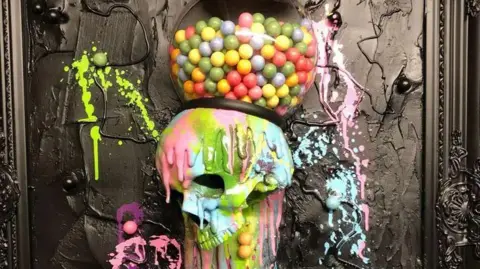 A colourful resin skull, with a gum ball machine on top