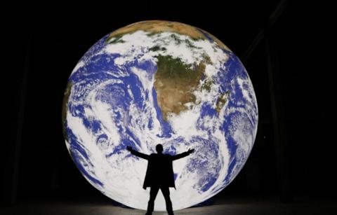 A man holding his arms out in front of a giant illuminated earth