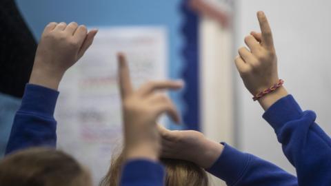 Pupils raise hands in a classroom