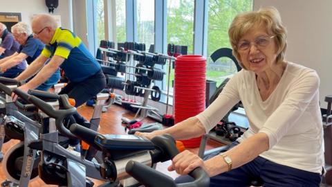 Lady with Parkinson's riding a bike in a gym spin class.