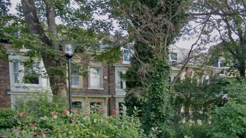 A row of Victorian terraced houses on a tree-lined street