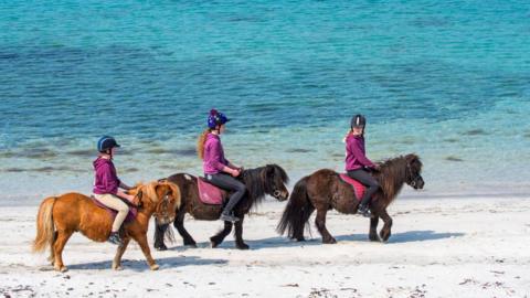 Three young girls riding ponies on beach in Shetland