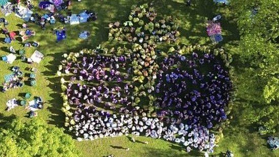 Image of people wearing yellow, purple and white ponchos making up the image of a crown