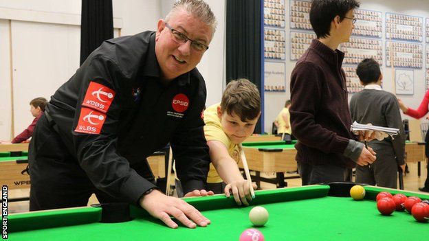 A young snooker player being coached.