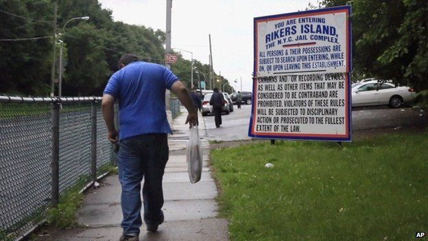 Man walks past Rikers Island entrance sign