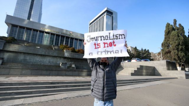 Журналист перед парламентом с плакатом "Журналистика - не преступление"
