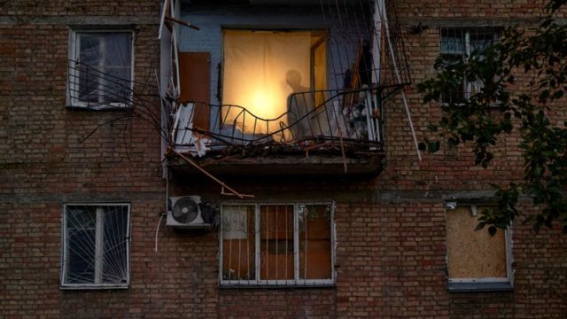 Тень человека за окном, занавешенным простыней, за поврежденным балконом