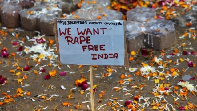 Плакат, на котором написано "Мы хотим Индии - свободной от изнасилованй" на земле среди разбросанных цветочных лепестков