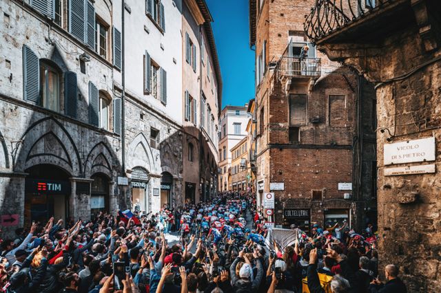 Зрители на узких улочках итальянского города Сиена наблюдают прохождение пелотона в гонке 12 этапа состязания Giro d'Italia в 2021 году.