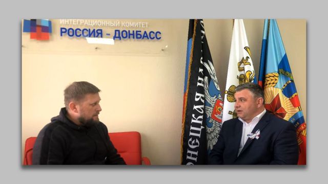 Логотип Интеграционного комитета Россия-Донбасс на стене над двумя мужчинами