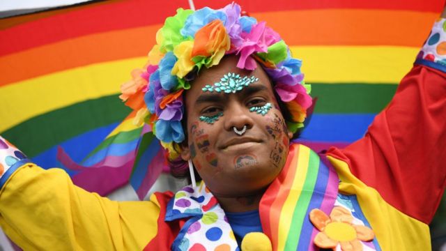 Участник парада в разноцветном венке на фоне радуги