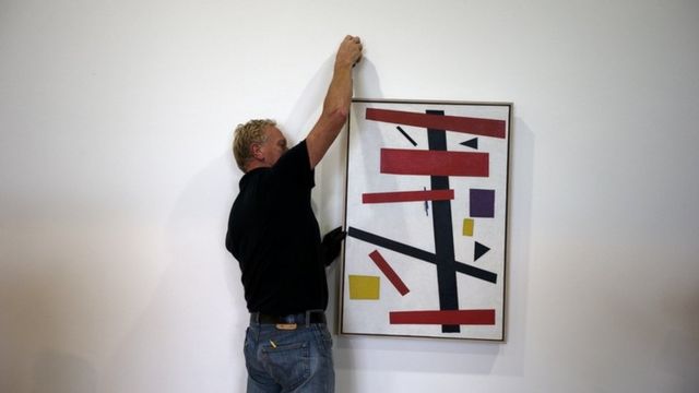 Мужчина вещает картину на стену музея