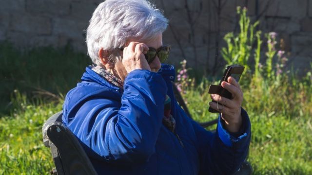 Пожилая женщина в очках смотрит на экран мобильного