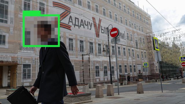 Москва. Неопознаваемый человек идет мимо здания с пропагандистским транспарантом